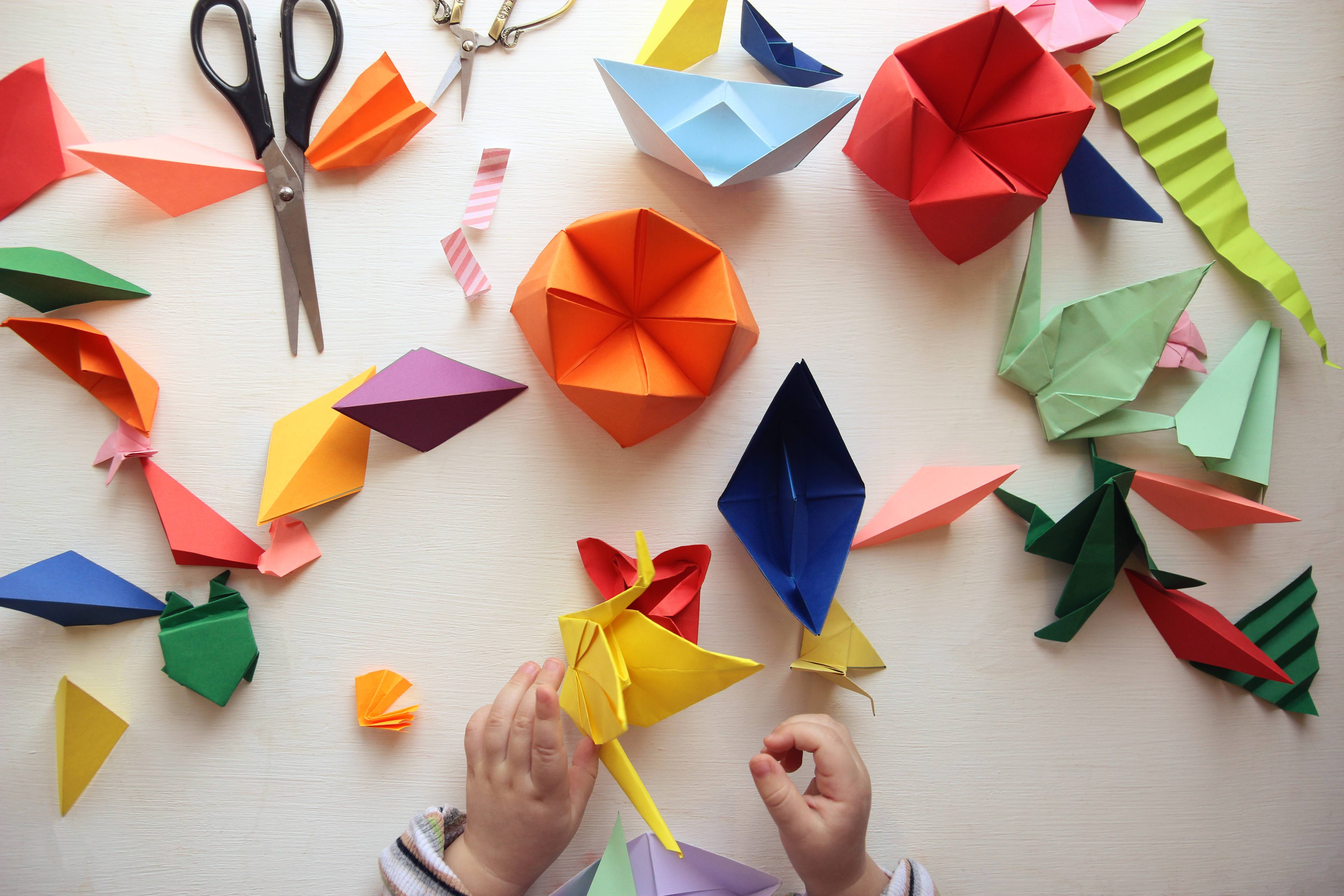 the child makes origami. Multicolored Origami and paper on  a white table. origami lesson