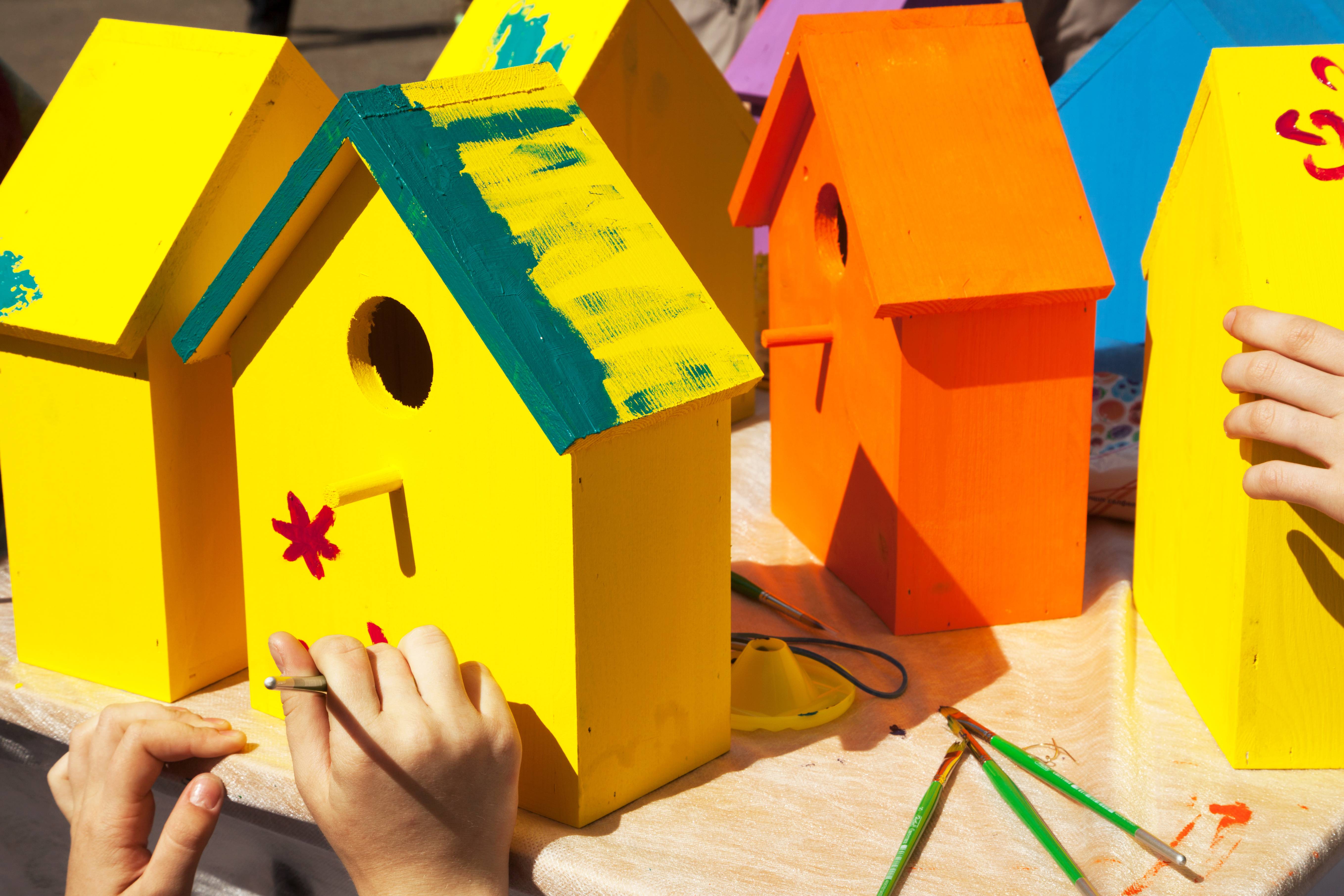 Children painting birdhouses bright colors of orange and yellow. Kids woodcraft lesson, making wooden houses for birds